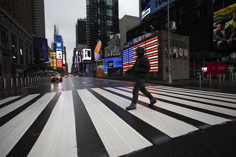 FILE - In this March 23, 2020, file photo, a man crosses the street in a nearly empty Times Square, which is usually very crowded on a weekday morning in New York. (AP Photo/Mark Lennihan, File)