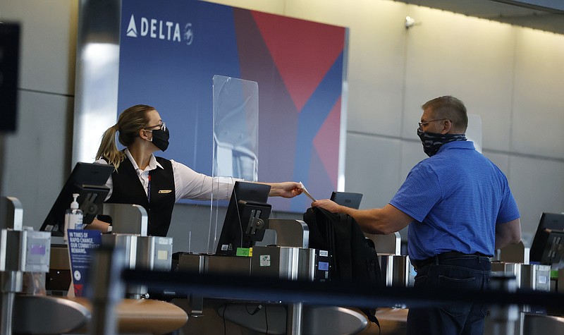 FILE - In this July 22, 2020 photo, a ticketing agent for Delta Airlines hands a boarding pass to a passenger as he checks in for a flight in the main terminal of Denver International Airport in Denver. Delta Air Lines will use its frequent flyer program to back up $6.5 billion in funding as the pandemic continues to buffet air travel. (AP Photo/David Zalubowski, File)