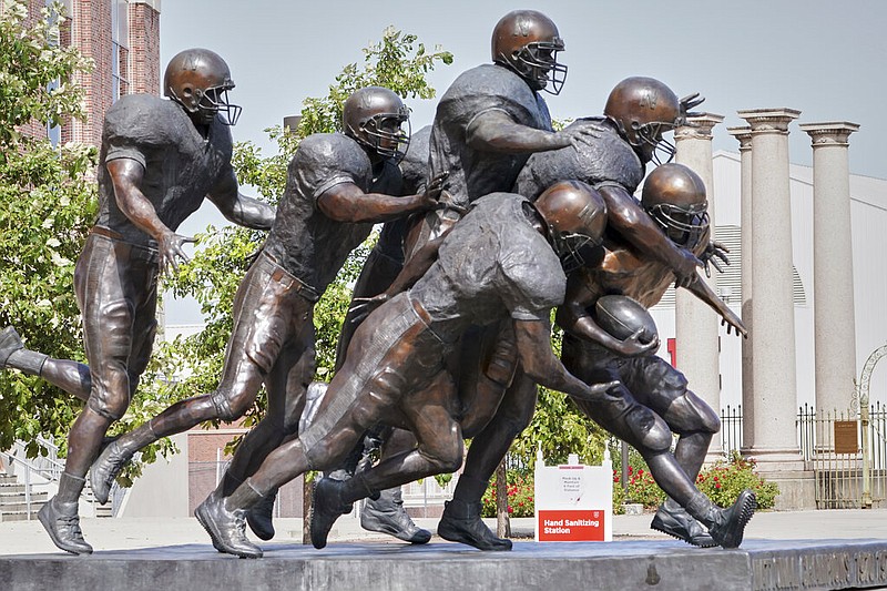 A hand sanitizing station is placed behind a statue of football players outside Memorial Stadium in Lincoln, Neb., Tuesday, Sept. 15, 2020. (AP Photo/Nati Harnik)
