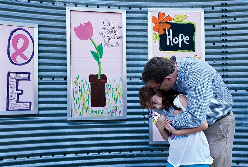 Marshall Wood hugs his daughter Haley on Sept. 11, 2012, in front of the Texarkana Regional Arts and Humanities Council's Art Wall during at an unveiling ceremony for paintings created by breast cancer survivors or family members who have lost loved ones to breast cancer.  Wood lost his mother to breast cancer, and Haley made a painting on the wall in her honor. (FILE PHOTO BY DOUG STRICKLAND)