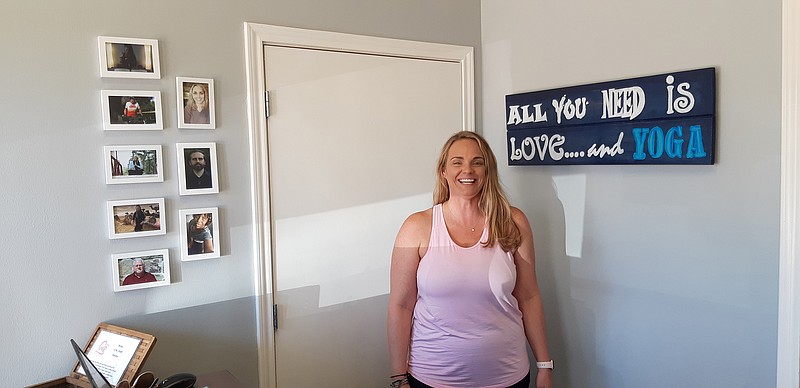 Lauren Booker, co-owner of One Love Yoga, stands in the reception area of her new studio. Though located just down the street from their original location, she says the new place is just what they needed as they experienced an influx of students over the last several months. She is standing between photos of her instructors and the studio's motto, "All you need is love ... and yoga."