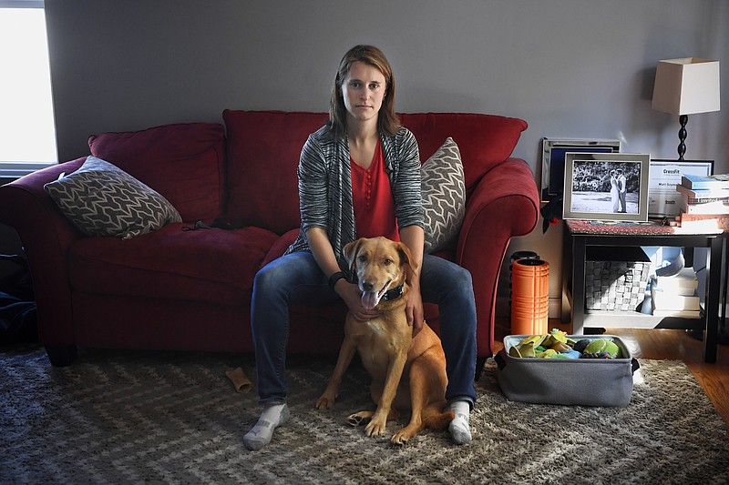 Melissa Wilhelm Szymanski sits with her dog Cooper at home in Glastonbury, Conn., on Saturday, Sept. 19, 2020. Wilhelm Szymanski got sick earlier this year and wound up with a $3,200 bill because she wasn't diagnosed initially with COVID-19. Even though dozens of insurers and the federal government are offering to pick up all treatment costs during the pandemic, many holes remain for big bills to surprise patients. (AP Photo/Jessica Hill)