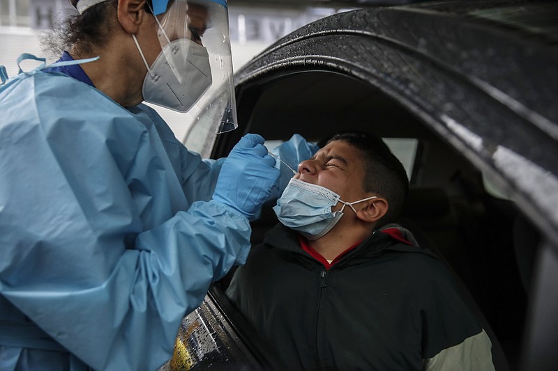 Medical staff takes a swabs as she tests a boy for COVID-19 at a drive-through at the San Paolo hospital, in Milan, Italy, Thursday, Oct. 15, 2020. Coronavirus infections are surging again in the region of northern Italy where the pandemic first took hold in Europe, renewing pressure on hospitals and health care workers. (AP Photo/Luca Bruno)