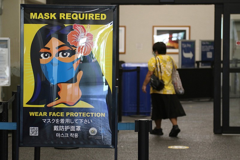 A woman walks into the international airport in Honolulu on Friday, Oct. 2, 2020. After a summer marked by a surge of coronavirus cases in Hawaii, officials plan to reboot the tourism based economy later this month despite concerns about the state's pre-travel testing program. (AP Photo/Caleb Jones)