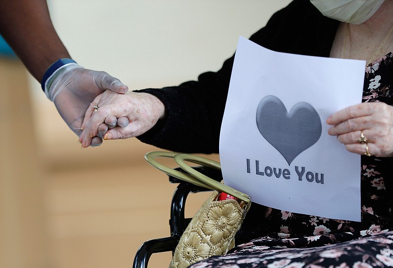 In this July 17, 2020 file photo, a senior citizen holds the hand of a care coordinator at a Health facility in Miami.  Federal health officials on Friday unveiled a plan to get approved coronavirus vaccines to nursing home residents free of cost, with the aid of two national pharmacy chains.
No vaccine has yet been approved by the Food and Drug Administration, and the distribution program is contingent on that happening first. (AP Photo/Wilfredo Lee)