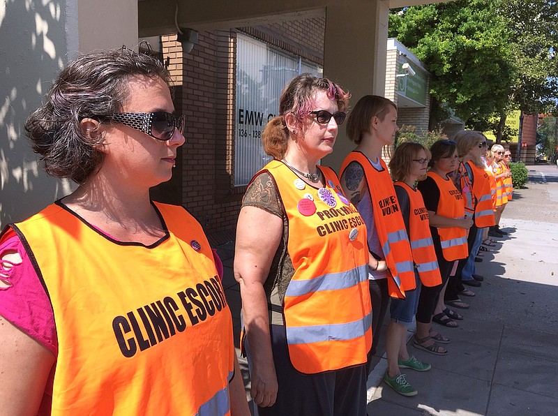 In this July 17, 2017 file photo, escort volunteers line up outside the EMW Women's Surgical Center in Louisville, Ky., the state's only abortion clinic. Kentucky's Attorney General Daniel Cameron, an anti-abortion supporter, said Friday, March 27, 2020, that abortions should cease as part of the governor's order halting elective medical procedures in the state due to the coronavirus pandemic. (AP Photo/Dylan Lovan, File)