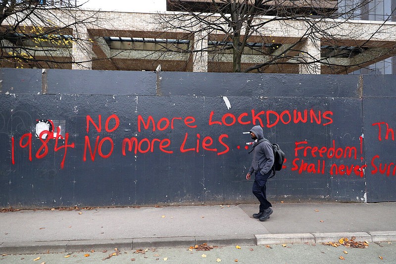 A man walks past anti-lockdown graffiti in Manchester, England, Monday, Oct. 19, 2020 as the row over Greater Manchester region's coronavirus status continues. Britain's government says discussions about implementing stricter restrictions in Greater Manchester must be completed Monday because the public health threat caused by rising COVID-19 infections is serious and getting worse. (Peter Byrne/PA via AP)