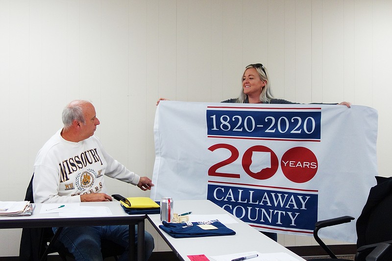 <p>Helen Wilbers/FULTON SUN Callaway 200 committee members Doc Kritzer, left, and Lisa Fansler show off a full-sized flag for the occasion in this pre-pandemic file photo. Callaway 200 merchandise and special Callaway County-themed wines will be on sale Saturday during Bicentennial Day at Serenity Valley Winery.</p>