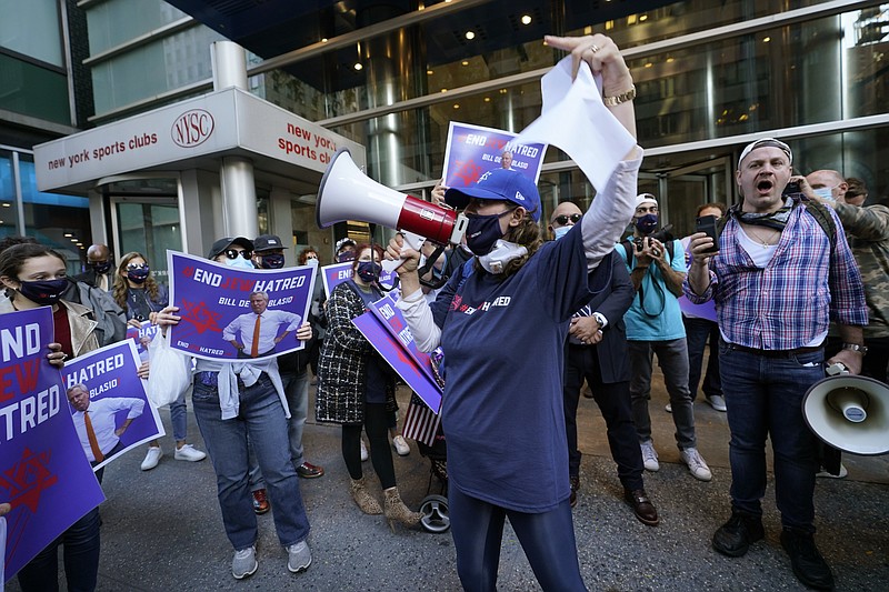 FILE - In this Oct. 15, 2020, file photo, protesters gather on the sidewalk outside the offices of New York Gov. Andrew Cuomo in New York. After shutdowns swept entire nations during the first surge of the coronavirus earlier this year, some countries and U.S. states are trying more targeted measures as cases rise again around the world. In New York City's borough of Brooklyn, Orthodox Jews have complained their communities are being singled out for criticism. (AP Photo/Kathy Willens)