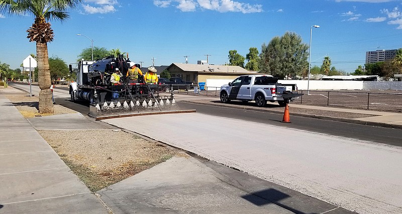 A City of Phoenix Street Transportation Department crew sprays light-colored pavement over blacktop on a street in the Garfield District of Phoenix on Aug. 11, 2020. A team from Arizona State University is working with the city of Phoenix on a pilot program studying the use of "cool pavement" to reduce heat island effect, a phenomenon that raises temperatures in urban areas covered by asphalt and concrete. (City of Phoenix via AP)