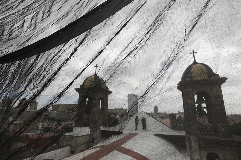 Men are seen through safety netting as they stand atop a less-damaged section of Nuestra Senora de Los Angeles, or Our Lady of Angels church, during the early stages of reconstruction work, three years after an earthquake collapsed nearly half of the church's 18th-century dome in Mexico City, Friday, Oct. 16, 2020. The experts working on projects like this across Mexico face some of the same issues confronting restorers everywhere, like France’s re-building of the Notre Dame Cathedral: are the materials and craftsmen's skills of centuries ago still available? (AP Photo/Rebecca Blackwell)