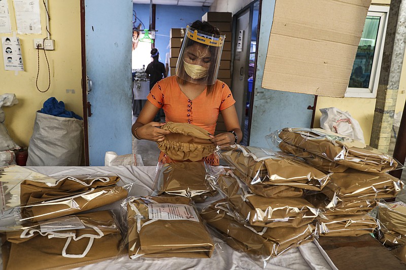 FILE - In this May 28, 2020, file photo, a woman wearing face mask and face shield to help curb the spread of the new coronavirus checks surgical gown at a packing session of a garment factory at Industrial Zone in Yangon, Myanmar. The coronavirus pandemic has slammed the apparel industry, leaving many of the 65 million Asian garment factory workers struggling as factories close or cut back on wages, and the International Labor Organization is urging the industry to do more to protect them. (AP Photo/Thein Zaw, File)