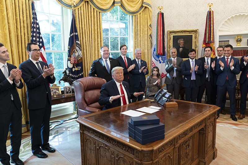 President Donald Trump reacts after hanging up a phone call with the leaders of Sudan and Israel, as Treasury Secretary Steven Mnuchin, second from left, Secretary of State Mike Pompeo, White House senior adviser Jared Kushner, National Security Adviser Robert O'Brien, and others applaud in the Oval Office of the White House, Friday, Oct. 23, 2020, in Washington. (AP Photo/Alex Brandon)