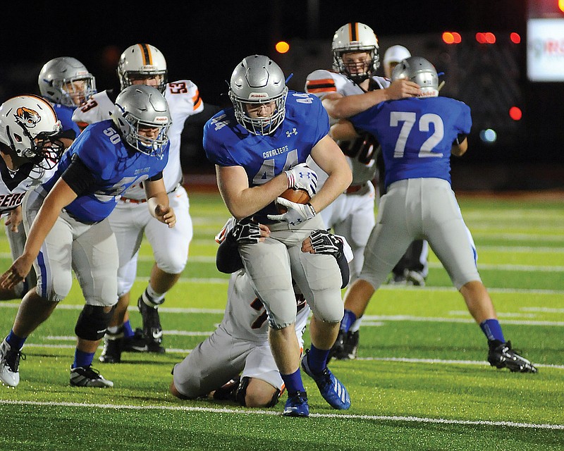 Ian Nelson of Capital City carries the ball while dragging a Kirksville defender behind him during Friday's game at Adkins Stadium. The Cavaliers won 13-7 for their first victory in program history.