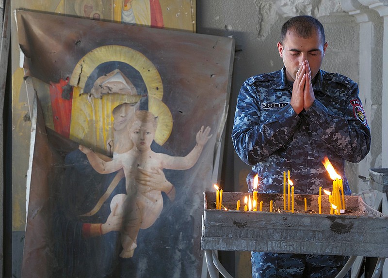 A policeman prays in the Holy Savior Cathedral, damaged by shelling by Azerbaijan's artillery during a military conflict in Shushi, the separatist region of Nagorno-Karabakh, Saturday, Oct. 24, 2020, with a damaged icon of the Virgin on the left. The heavy shelling forced residents of Stepanakert, the regional capital of Nagorno-Karabakh, into shelters, as emergency teams rushed to extinguish fires. Nagorno-Karabakh authorities said other towns in the region were also targeted by Azerbaijani artillery fire. (AP Photo)