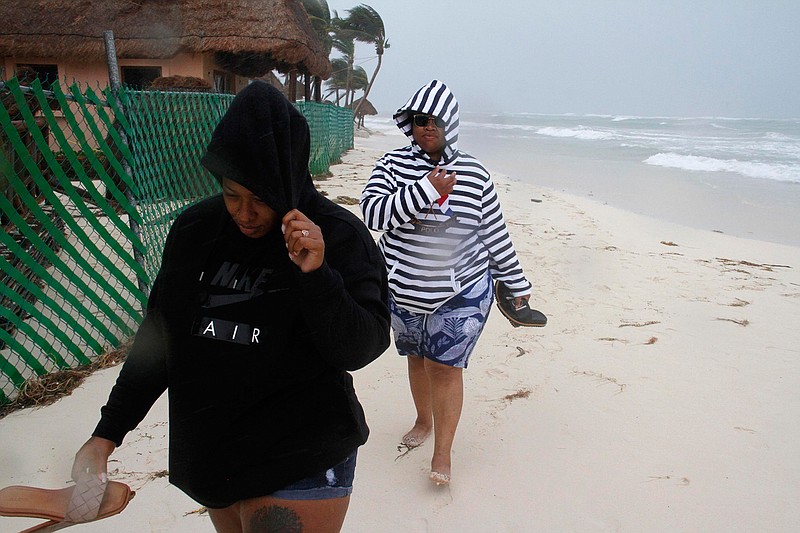 Tourists walk on the beach as the tail end of Hurricane Zeta makes landfall in Playa del Carmen, Mexico, early Tuesday, Oct. 27, 2020. Zeta is leaving Mexico's Yucatan Peninsula on a path that could hit New Orleans Wednesday night. (AP Photo/Tomas Stargardter)
