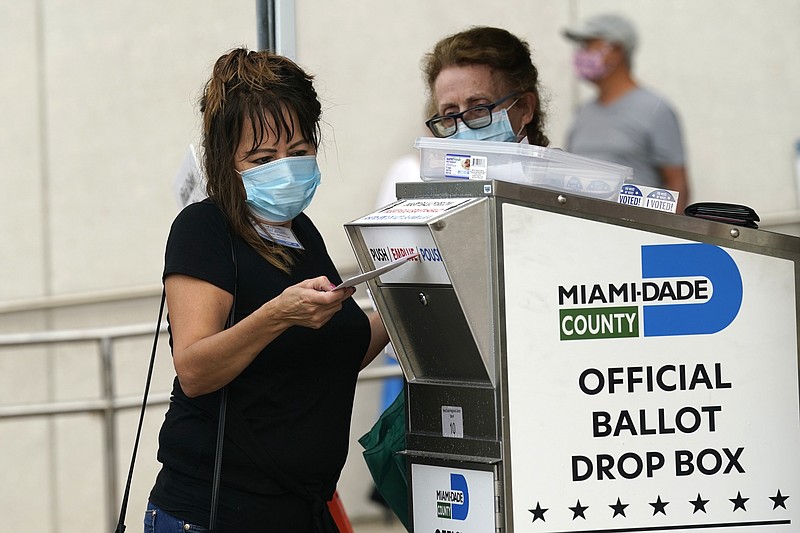 FILE - In this Monday, Oct. 19, 2020, file photo, an election worker places a vote-by-mail ballot into an official ballot drop box outside of an early voting site, in Miami. Just days before the presidential election, millions of mail-in ballots have still not been returned in key battleground states. Many of those are due in county offices by Tuesday, Nov. 3, but the latest Postal Service delivery data suggests it’s too late for voters to drop their ballots in the mail. (AP Photo/Lynne Sladky, File)