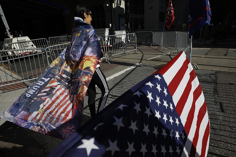 A woman wears a Trump flag as a cape as supporters of President Donald Trump protest outside the Pennsylvania Convention Center, where vote counting continues, in Philadelphia, Monday, Nov. 9, 2020, two days after the 2020 election was called for Democrat Joe Biden.  (AP Photo/Rebecca Blackwell)