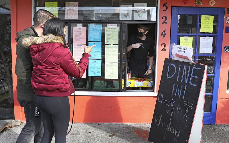 Senor Moose server and bartender Phil West, right, confirms there is indoor brunch seating for married couple Nataly Ocampo, 28, and Stephen Durkee, 36, shortly after Washington Gov. Jay Inslee's executive orders to stop indoor restaurant dining in the coming days to combat Covid-19, Sunday, Nov. 15, 2020, in Seattle's Ballard neighborhood. West, a long time employee at the restaurant, said the "Dine In!" sign had just been made, and that this is the first time the restaurant allowed inside dining since March. It has allowed sidewalk dining for a while and will continue. "It's probably a good thing to shut down for public safety," said West, who at first said, "It's not ideal." Senor Moose will remain open for takeout and sidewalk dining.  (Ken Lambert /The Seattle Times via AP)