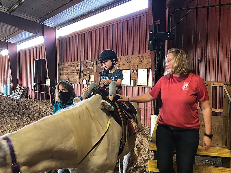 Runnin WJ Riding Ranch Program Director Brittany Rogers, right, helps a young rider keep steady as he eagerly awaits his ride. The ranch reopened earlier this month after having to close down because of the coronavirus.