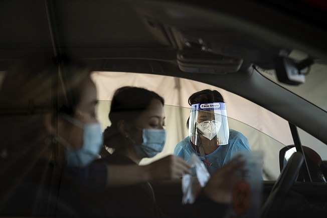 Medical assistant Linh Nguyen assists two women with COVID-19 testing at a testing site set up at the OC Fairgrounds in Costa Mesa, Calif., Monday, Nov. 16, 2020. (AP Photo/Jae C. Hong)