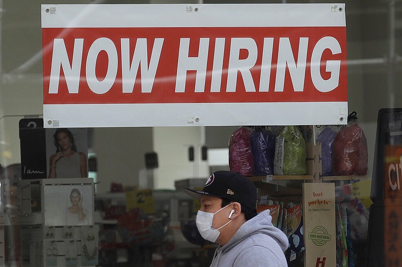 This May 7, 2020, file photo shows a man wearing a mask while walking under a Now Hiring sign at a CVS Pharmacy during the coronavirus outbreak in San Francisco.