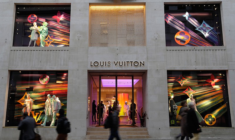 In this Monday, Nov. 25, 2019 file photo, pedestrians pass a Louis Vuitton shop window in London. Sales of luxury apparel, jewelry and beauty products are set to slide by nearly a quarter this year as the pandemic wipes out more than six years of growth, according to a study released Wednesday, Nov. 18, 2020 by the consultancy Bain. (AP Photo/Kirsty Wigglesworth, File)