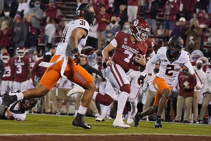 Oklahoma quarterback Spencer Rattler (7) carries for a touchdown, between Oklahoma State's Kolby Harvell-Peel (31) and Tanner McCalister (2) during the first half of an NCAA college football game in Norman, Okla., Saturday, Nov. 21, 2020. (AP Photo/Sue Ogrocki)