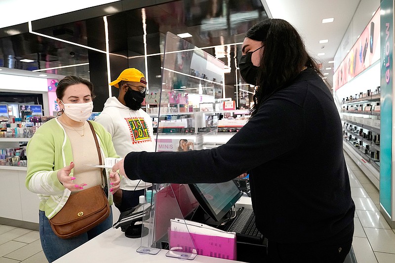 Cashier Druhan Parker, right, works behind a plexiglass shield Thursday, Nov. 19, 2020, as he checks out shoppers Cassie Howard, left, and Paris Black at an in Chicago. The accelerating surge of coronavirus cases across the U.S. is causing an existential crisis for America's retailers and spooking their customers just as the critically important holiday shopping season nears. (AP Photo/Charles Rex Arbogast)