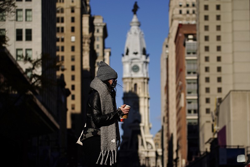 In this Nov. 18, 2020 photo, a person wearing a face mask crosses Broad Street in Philadelphia. As governors and mayors grapple with an out-of-control pandemic, they are ratcheting up mask mandates and imposing restrictions on small indoor gatherings, which have been blamed for accelerating the spread of the coronavirus. (AP Photo/Matt Slocum)