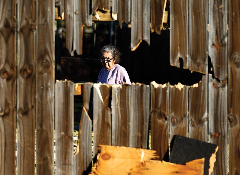 A woman looks through the hole in her fence as she inspects the damage in her yard following the tornado-warned storm Tuesday evening. City of Arlington street crews were cleaning up debris along Pioneer Parkway in Arlington, Texas Wednesday, Nov. 25, 2020. (Tom Fox/The Dallas Morning News via AP)