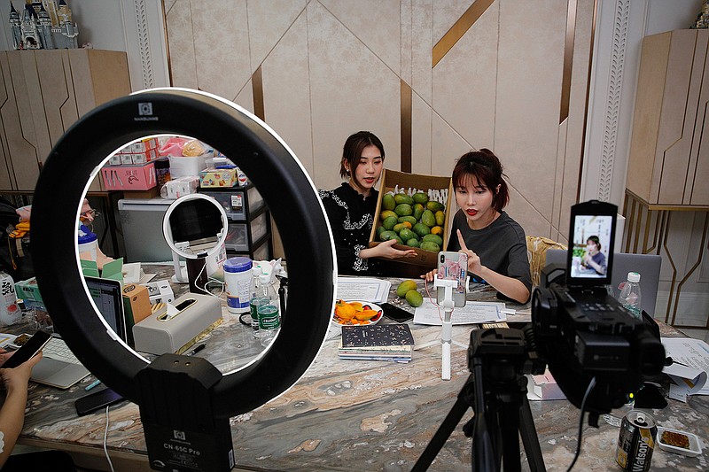 FILE - In this May 5, 2020, photo, China's online celebrity Zhang Mofan, right, introduces fresh mangos to her online clients and fans through the live-streaming at her house in Beijing.  Livestream selling, already popular in China, is taking off in the U.S., ushering in a new way for Americans to shop online. Instead of searching for what they want, they pick up their phones, sit back, and click to buy if they like what they see.(AP Photo/Andy Wong)