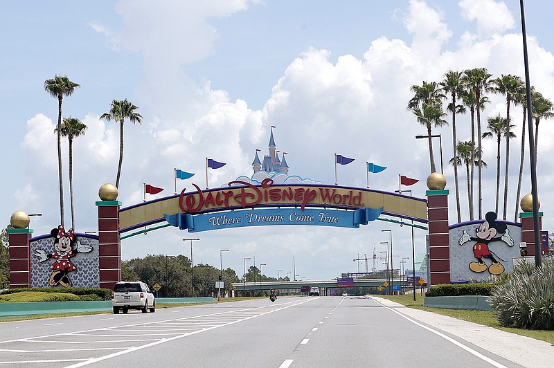 In this Thursday, July 2, 2020, file photo, cars drive under a sign greeting visitors near the entrance to Walt Disney World, in Lake Buena Vista, Fla.   The Walt Disney Co. is announcing plans to lay off 4,000 more workers in its theme parks division in California and Florida due to the COVID-19 pandemic's effect on the industry. The company has been limiting attendance at its parks and changing protocols to allow for social distancing. (AP Photo/John Raoux, File)