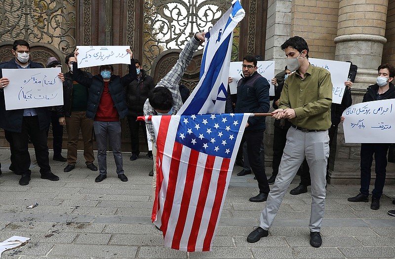 Two protesters burn the representation of the U.S. and Israeli flags as the others hold placards condemning inspections by the UN nuclear agency (IAEA) on Iran's nuclear activities and the country's nuclear talks with world powers during a gathering in front of Iranian Foreign Ministry on Saturday, Nov. 28, 2020 in Tehran.  Supreme Leader Ayatollah Ali Khamenei is calling for "definitive punishment" of those behind killing of Mohsen Fakhrizadeh, the scientist linked to Tehran's disbanded military nuclear program. (AP Photo/Vahid Salemi)