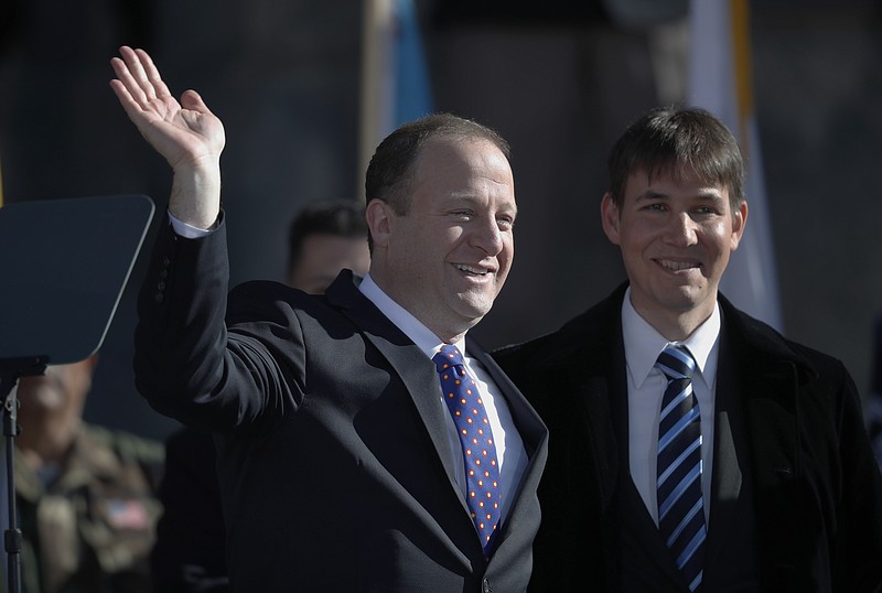 FILE - In this Tuesday, Jan. 8, 2019 file photo, Colorado Gov. Jared Polis, left, joins his partner, Marlon Reis, in acknowledging the crowd after Polis took the oath of office during the inauguration ceremony in Denver. Colorado Gov. Jared Polis has tested positive for the coronavirus. Polis and his partner, Marlon Reis, both have COVID-19 and are asymptomatic, the governor said in a statement Saturday night, Nov. 28, 2020.  (AP Photo/David Zalubowski, Pool)