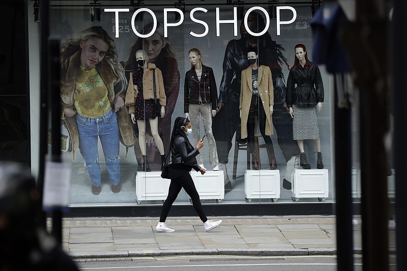 FILE - In this file photo dated Friday, Nov. 20, 2020, a woman wearing a face mask walks past mannequins wearing face masks in the window of a temporarily closed branch of the Topshop women's clothing chain during England's second coronavirus lockdown, in London.  Some 15,000 retailing jobs in Britain are in peril after Arcadia Group, owner of some of the country's best-known fashion chains like Topshop, confirmed Friday Nov. 27, 2020, that it is in talks about its future. (AP Photo/Matt Dunham, FILE)
