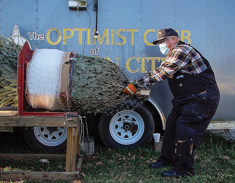 Walt Shull pulls a tree through a cylindrical tree wrapper for a customer Friday at the Jefferson City Optimist Club's annual Christmas tree sale lot along Dunklin Street. The wrapper, a simple machine that neatly packs the trees in plastic netting, assures the tree can be safely packed atop a car and driven to its new home.