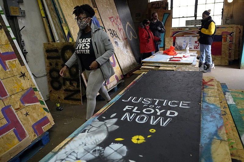 Leesa Kelly, left, walks past plywood mural boards as she and Kenda Zellner-Smith, background right, and volunteers meet at a warehouse, Saturday, Dec. 12, 2020, in Minneapolis to organize them. The two women formed the Save the Boards to Memorialize the Movement to preserve the painted expressions and pain born of outrage after the death of George Floyd at the hands of Minneapolis police in May. (AP Photo/Jim Mone)