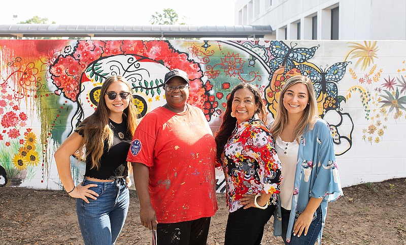 Ashley Wright, left, Darlene Taylor, Irma Wright and Allison Wright pose in front of the mural Taylor is painting for the Wright family's new business venture. The mural will span several walls and buildings to create an interactive piece. Irma Wright, the owner of the property, met Taylor after she inquired about who was painting the holiday window murals at Lowe's in Texarkana several years ago. Since then, Taylor has helped Wright with several art projects.