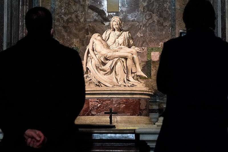 Visitors admire the marble sculpture "The Piety", made in 1499 by Italian sculptor Michelangelo Buonarroti, inside St. Peter's Basilica, at the Vatican, Monday, Dec. 14, 2020. Like elsewhere in Europe, museums and art galleries in Italy were closed this fall to contain the spread of COVID-19, meaning art lovers must rely on virtual tours to catch a glimpse of the treasures held by famous institutions such as the Uffizi in Florence and the Vatican Museums in Rome. However, some exquisite gems of Italy's cultural heritage remain on display in real life inside the country's churches, some of which have collections of renaissance art and iconography that would be the envy of any museum. (AP Photo/Andrew Medichini)