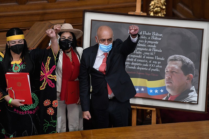 Jorge Rodriguez, right, lifts his fist after being sworn-in as president of the National Assembly, in front of a photo of late President Hugo Chavez, at Congress in Caracas, Venezuela, Tuesday, Jan. 5, 2021. The ruling socialist party assumed the leadership of Venezuela's congress, the last institution in the country it didn't already control. (AP Photo/Matias Delacroix)