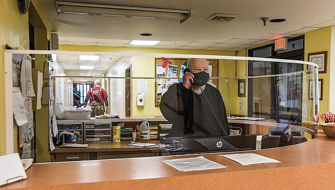 Center of Hope Shelter Manager Mike Cahalin takes a phone call from behind a circular-shaped plexiglass barrier at the front desk. Salvation Army staff have been making changes to keep up with requirements to keep staff and residents COVID-19 free.