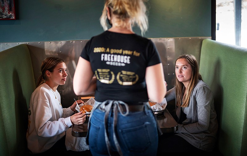 In this Jan. 11, 2021, file photo, Grace Mathre, server at Longfellow Grill, checks on University of St. Thomas students Lindsey Schulz and Maren Daggett in Minneapolis. As the U.S. finds itself in the most lethal phase of the coronavirus outbreak yet, governors and local officials in hard-hit parts of the country are showing little willingness to impose any new restrictions on businesses to stop the spread. (Glen Stubbe/Star Tribune via AP, File)