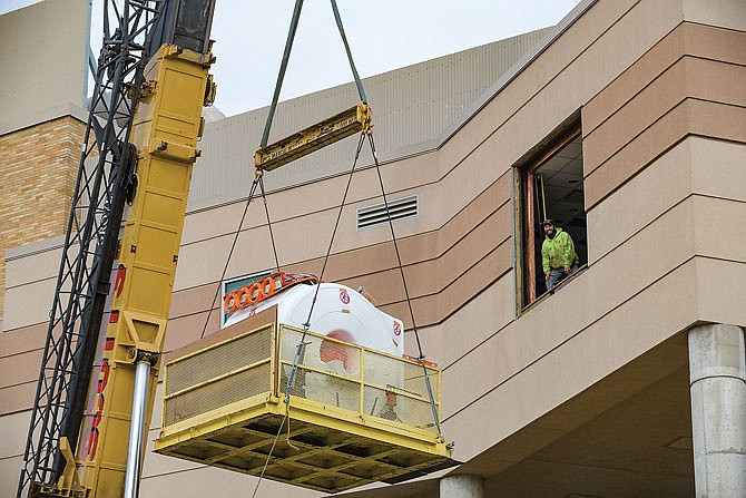 Bub Dooling stands in the open window as co-workers from Scott's Crane Service in Holts Summit and Simon Hegele Healthcare Solutions combine efforts to hoist a MAGNETOM Sola, a 1.5 Tesla magnetic resonance imaging machine weighing 7 tons into a second floor window at Capital Region Medical Center. The unit and its operating software is designed to increase productivity and decrease rescans for improved efficiency and patient satisfaction. The machine itself was lowered from the trailer on which it was transported here then onto a cookie sheet. It was then raised to the window opening and safely lowered into the room where Simon Hegele, of Wood Dale, Illinois, staff will set up the equipment.