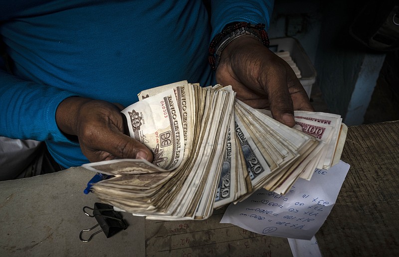 FILE - In this Dec. 11, 2020 file photo, a worker shows a wad of Cuban pesos in Havana, Cuba, Friday, Dec. 11, 2020. In 2021, the government is implementing a deep financial reform that reduces subsidies, eliminates a dual currency that was key to the old system, and raises salaries, in hopes of boosting productivity to help alleviate an economic crisis and reconfigure a socialist system that will still grant universal benefits such as free health care and education. (AP Photo/Ramon Espinosa, File)