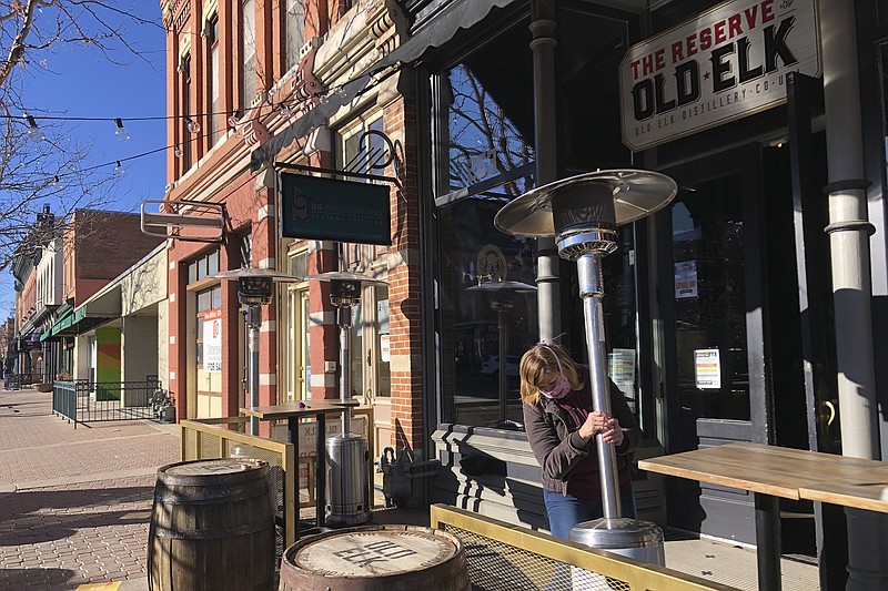 Whiskey tasting room manager Melinda Maddox moves a propane-fueled outdoor space heater in downtown Fort Collins, Colo., in preparation for opening on Wednesday, Jan. 6, 2021. Maddox and other bar and restaurant managers say they've sometimes struggled to find propane necessary for space heaters while they seat customers outside to comply with coronavirus public health restrictions. (AP Photo/Mead Gruver)