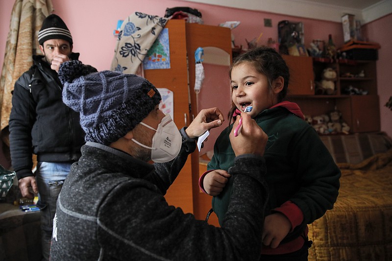 A little girl gets help from Valeriu Nicolae to learn brushing his teeth correctly as her father watches n Nucsoara, Romania, Saturday, Jan. 9, 2021. The rights activist has earned praise for his tireless campaign to change for the better the lives of the Balkan country’s poorest and underprivileged residents, particularly the children. (AP Photo/Vadim Ghirda)