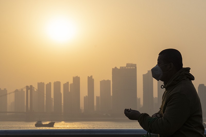 FILE - In this Jan. 15, 2021, file photo, a man wearing a mask is silhouetted as the sun sets along the riverbank in Wuhan in central China's Hubei province. Nearly a year to the day after Wuhan went into lockdown to contain a virus that had already escaped, President Joe Biden began putting into effect a new war plan for fighting the outbreak in the United States, Germany topped 50,000 deaths, and Britain closed in on 100,000. (AP Photo/Ng Han Guan)