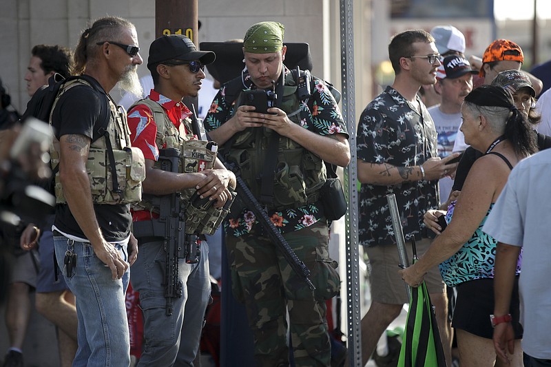 FILE - In this June 20, 2020 file photo, gun-carrying men wearing Hawaiian print shirts associated with the boogaloo movement watch a demonstration near where President Trump had a campaign rally in Tulsa, Okla. People following the anti-government boogaloo movement, which promotes violence and a second U.S. civil war, have been showing up at protests across the nation armed and wearing tactical gear. But the movement has also adopted an unlikely public and online symbol: Hawaiian print shirts.  (AP Photo/Charlie Riedel, File)