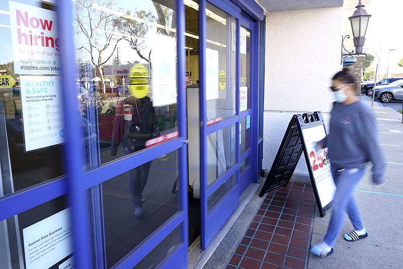 A customer walks by a "Now hiring" sign as she enters a Staple's store, Tuesday, Feb. 2, 2021, in Simi Valley, Calif.  Hiring has weakened for six straight months. Nearly 10 million jobs remain lost since the coronavirus struck. And this week, the Congressional Budget Office forecast that employment won’t regain its pre-pandemic level until 2024.  (AP Photo/Mark J. Terrill)